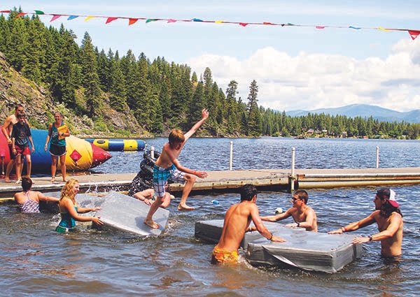 Campers playing in the water of Davis Lake and jumping off floating dock pads at Camp Spalding.