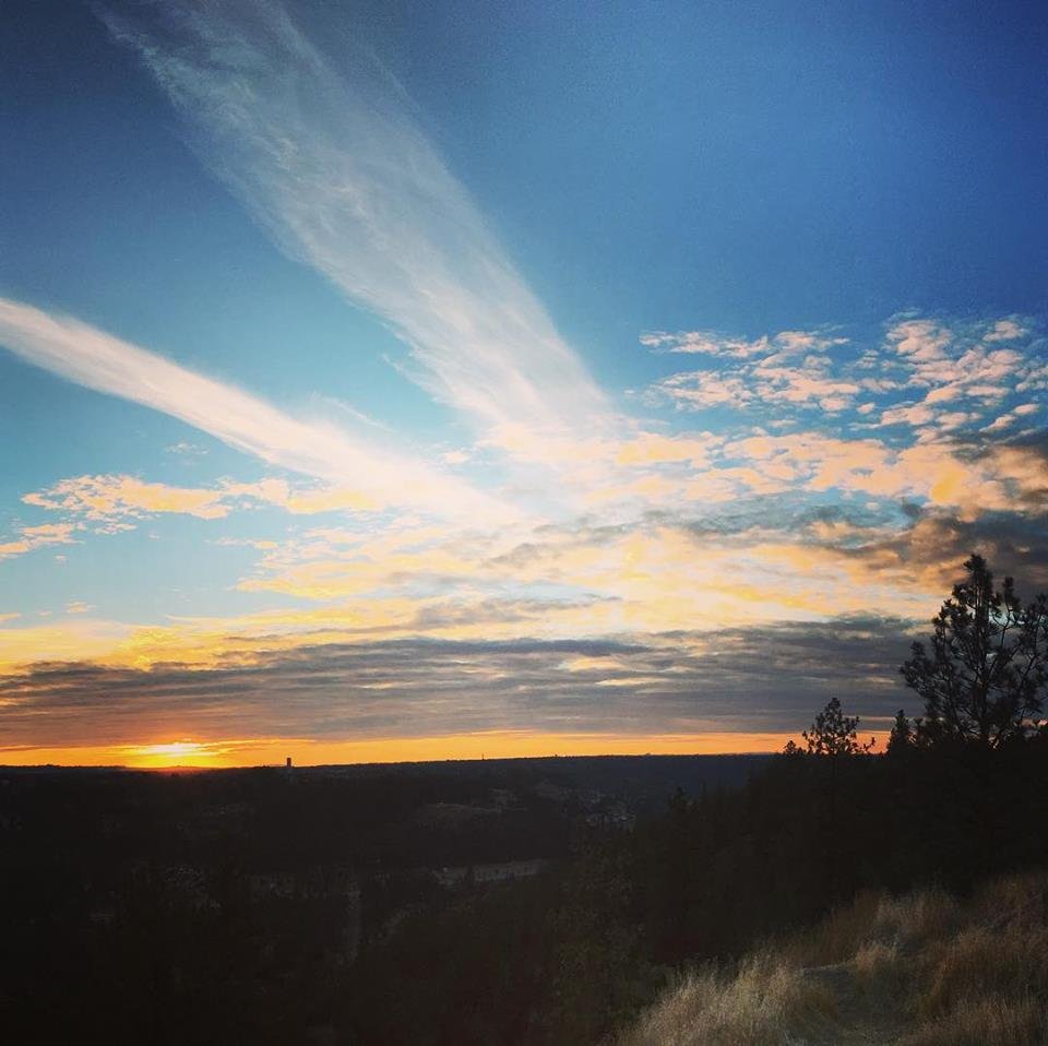 Sunset view and blue sky with streaks of white clouds radiating from ridge line horizon.