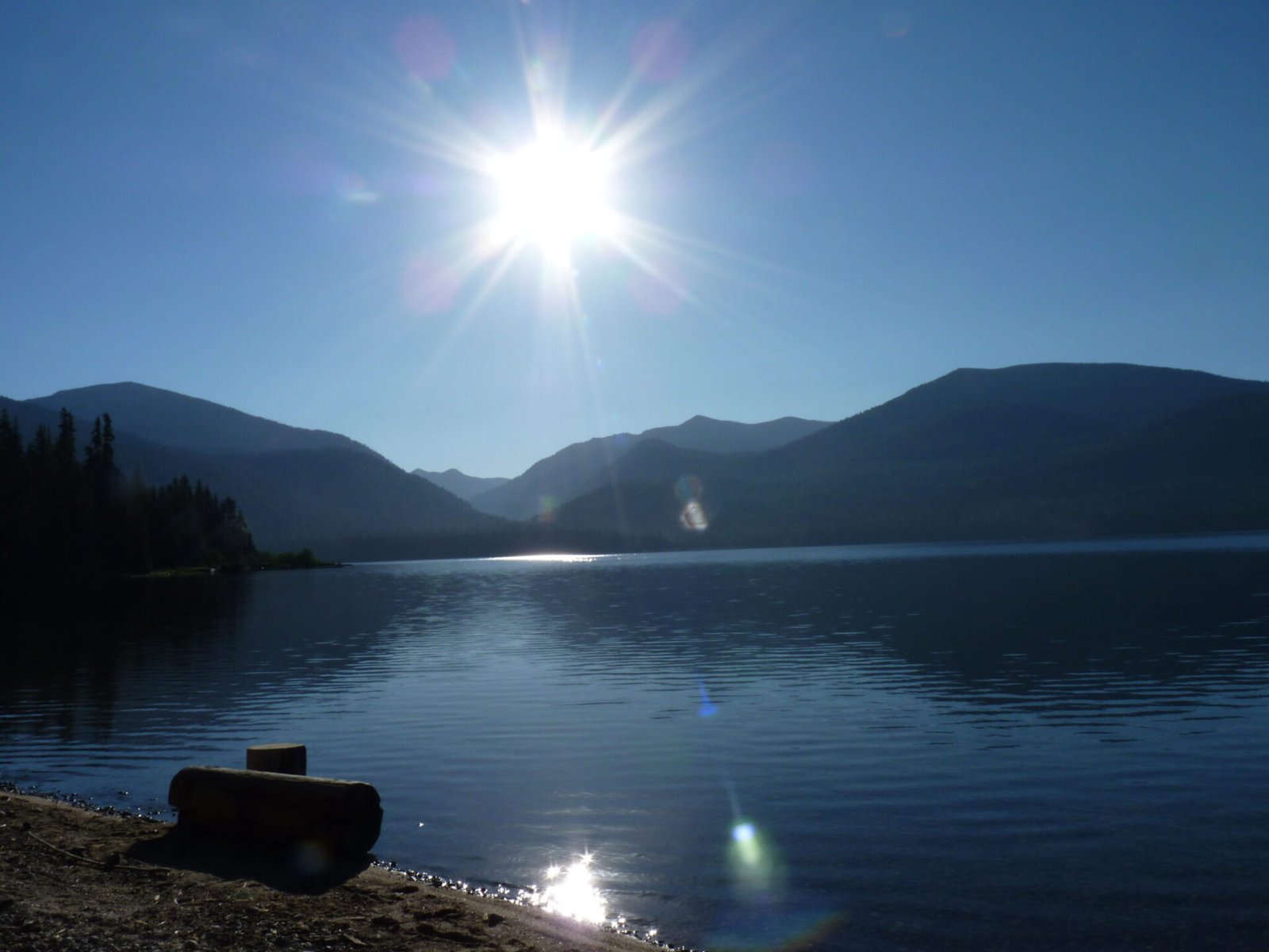 Still water of Priest Lake with mountain peaks and sun in the background.