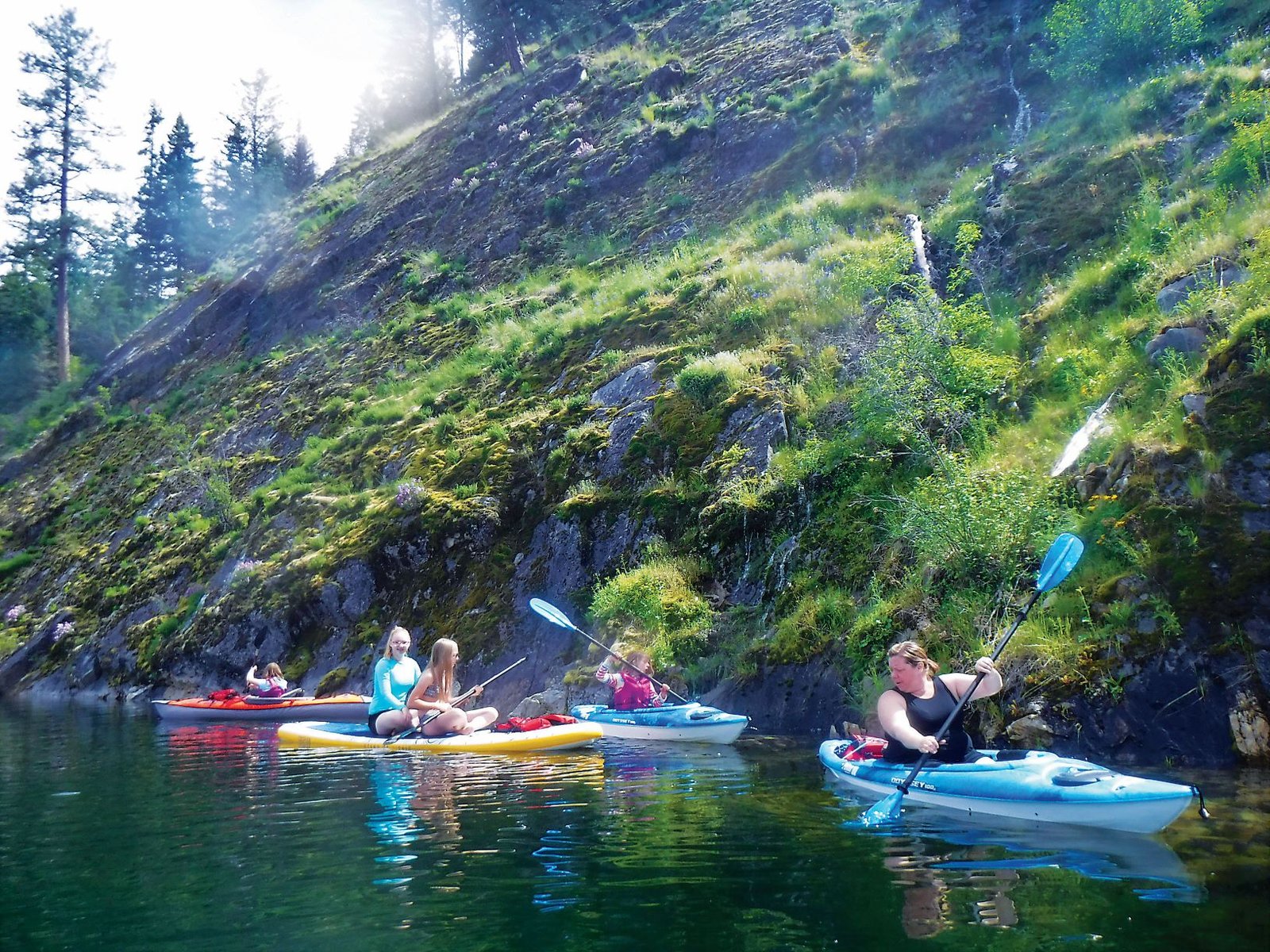 Mom and children kayaking near a rock cliff shoreline at Sullivan Lake.