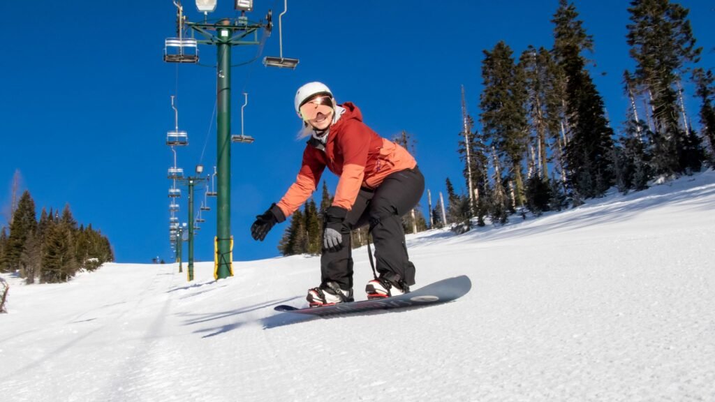 Woman snowboarding down a groomed run under a chairlift.