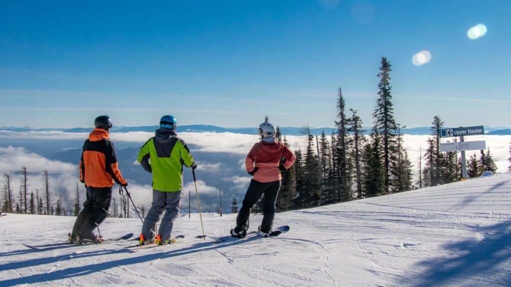 Two skiers and a snowboarder standing at the top of a run looking off to the horizon landscape of the surrounding mountain peaks.