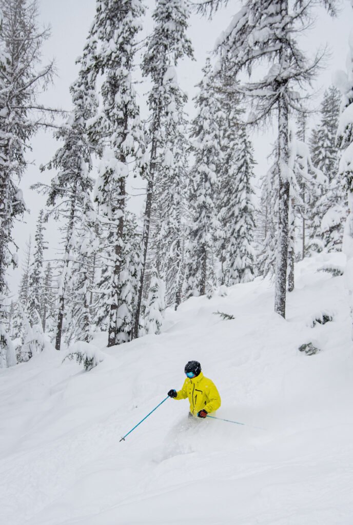 Skier in a yellow jacket going down a run with knee-deep powder snow.