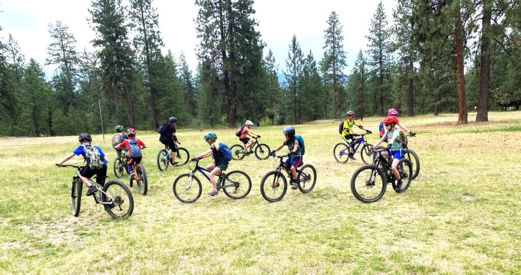 Youth mountain bike campers practicing riding techniques while riding in a circle over dirt and grass.