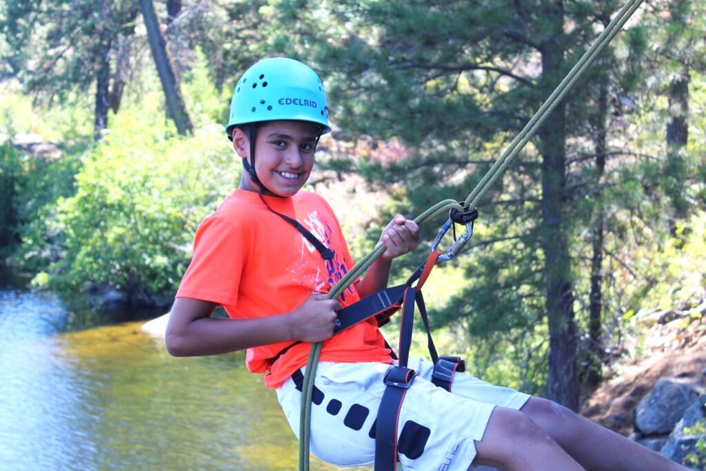 Child wearing safety helmet and harness while rappelling off rock face near the lake at Camp Spalding.