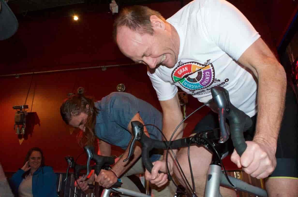 Two men pedal on stationary bikes in a race off.