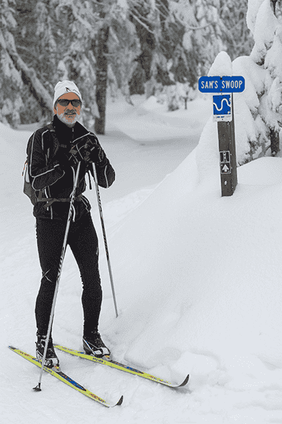 Photo of Sam Schlieder in front of trail sign for Sams Swoop.