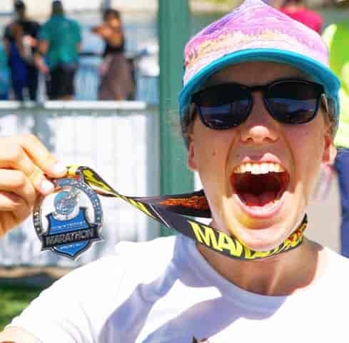 A woman holds a windermere marathon medal around her neck.