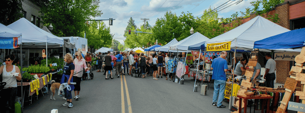 Photo of farmers market with people shopping at various stalls.