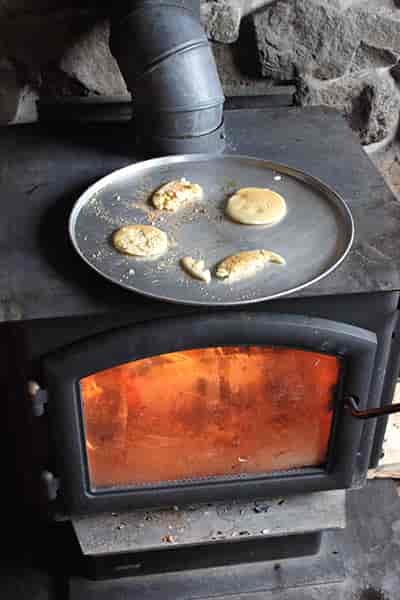 Photos of pancakes in skillet on top of wood burning stove.