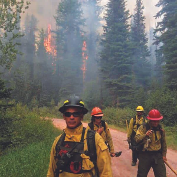 Photo of firefighters on dirt path in front of fire.