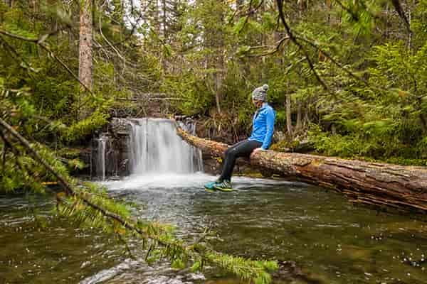 Photo of hiker sitting on log overhanging pool of water at base of a small waterfall.