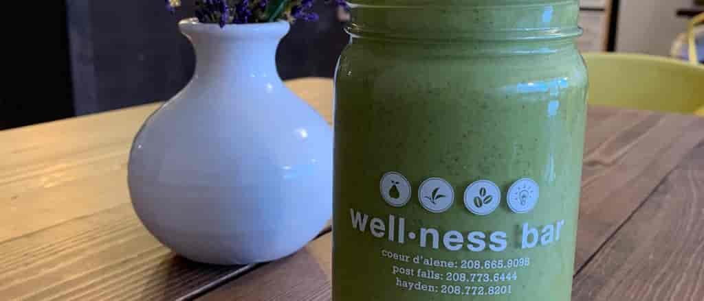 Photo of green smoothie in mason jar and vase on table.