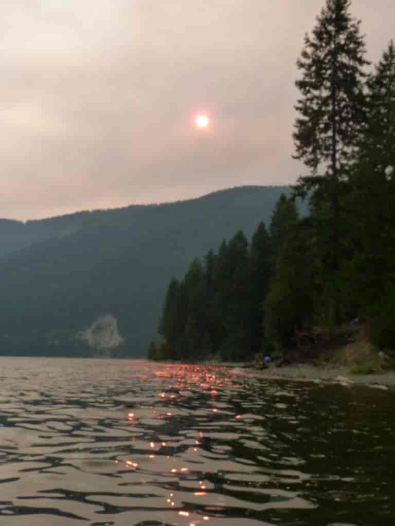 Wildfire smoke at Sullivan Lake obscures the sun, making it appear pink.