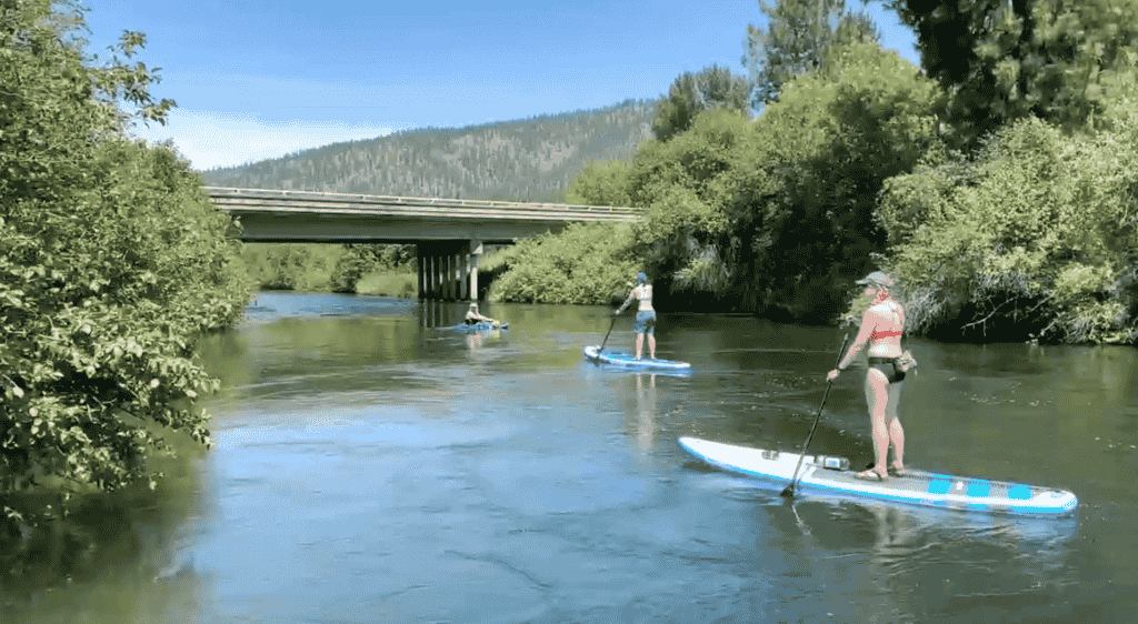 Two people paddle-boarding and one kayaking down a river.