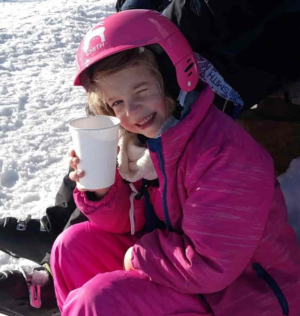 Girl winking while drinking hot cocoa outside in the snow.