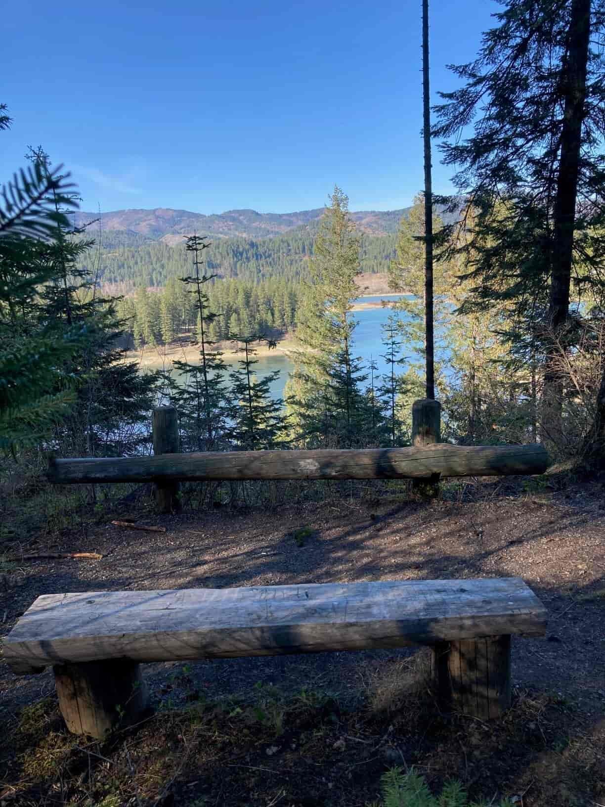 Viewpoint along Wolf Trails, with a wooden bend and trees, overlooking the Pend Oreille River with distant mountain slopes.