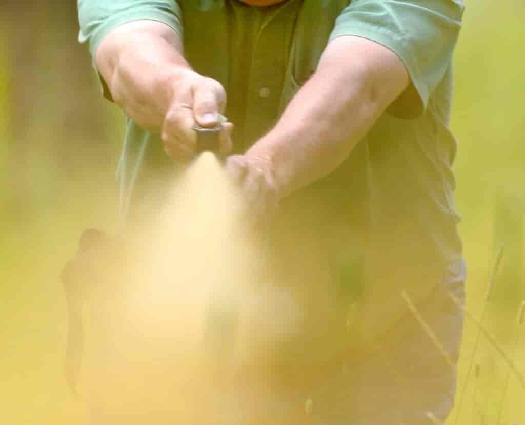 Close-up view of Chuck Bartlebaugh holding a can of bear spray with outstretched arms, with thumb pressing on top of spray can, demonstrating how to deploy bear repellent spray during a training session.